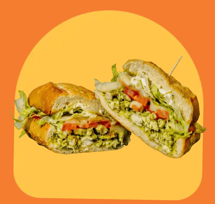A cross-section of a sub sandwich revealing pesto chicken, fresh lettuce, diced tomatoes, and creamy mayonnaise on a crusty roll.